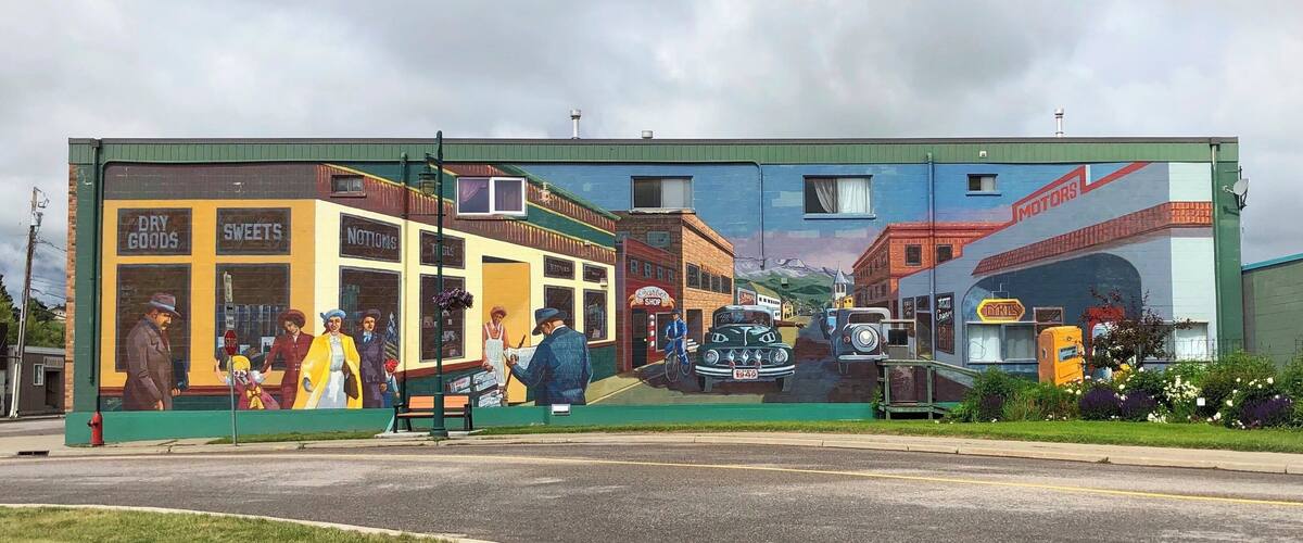 A mural of a street scene with vintage cars, people, and shops.