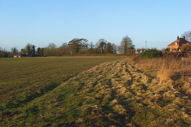 A rural landscape with a field, a house, and trees in the background.