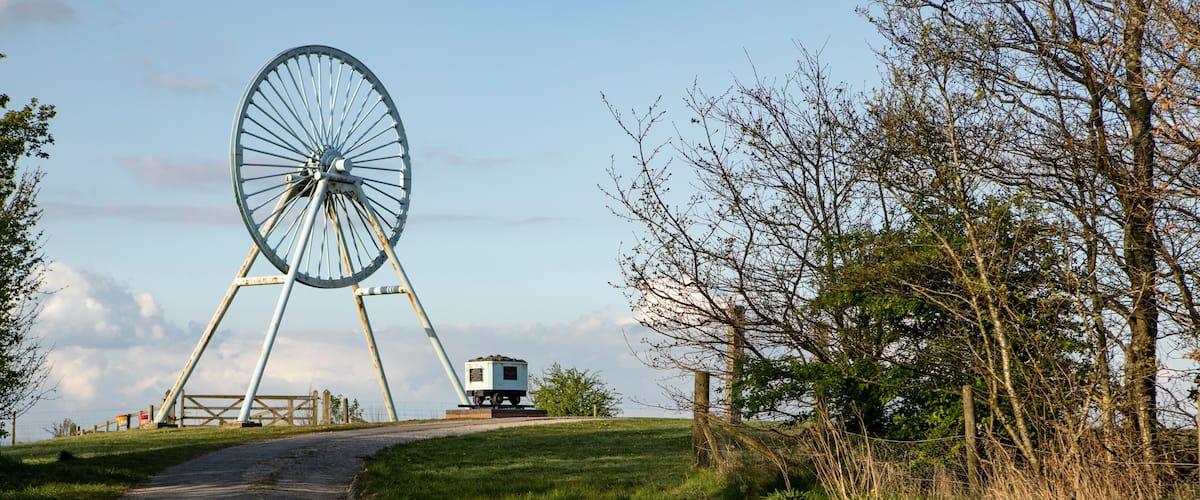 A dirt path leading to a large Ferris wheel, with a small building nearby.