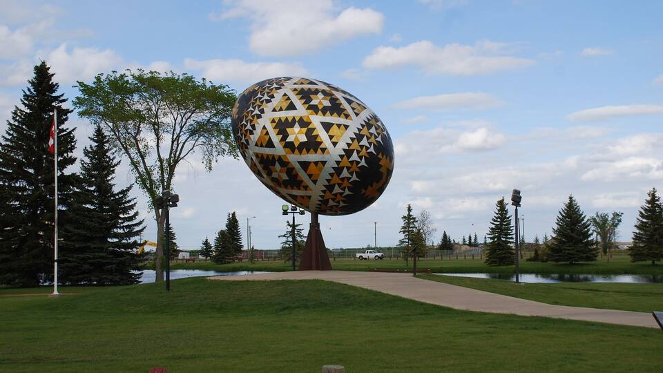 A large decorative sphere with star patterns in a park with trees and a pathway.