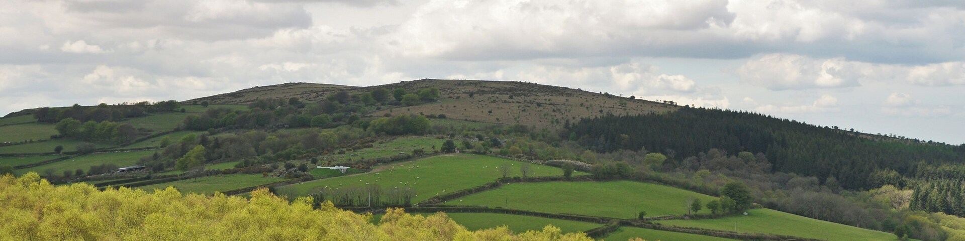 Rolling hills, green fields, and a cloudy sky.