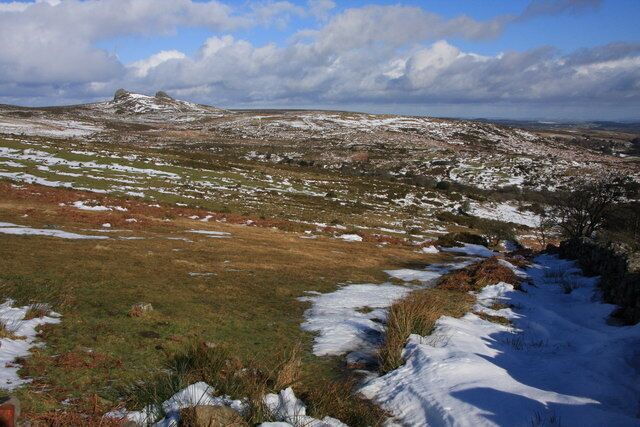 A snow-covered landscape with a rocky outcrop in the foreground and a distant mountain range under a partly cloudy sky.