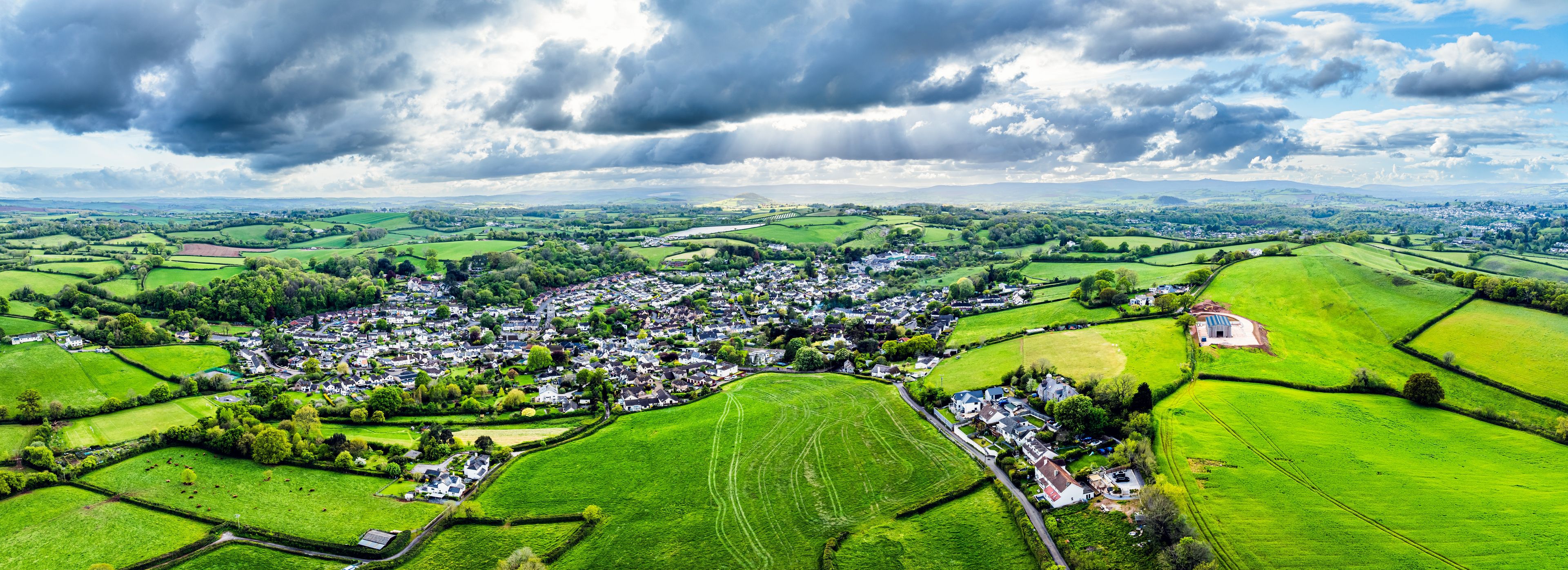 A rural landscape with a village, green fields, and a cloudy sky.