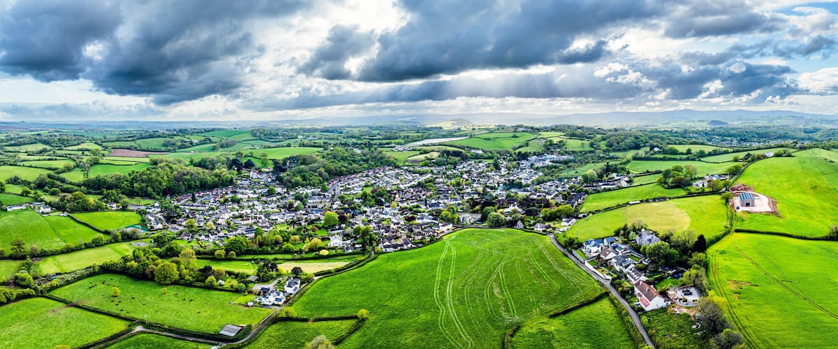 A rural landscape with a village, green fields, and a cloudy sky.