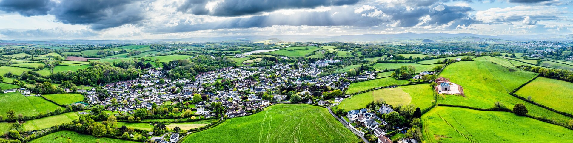 A rural landscape with a village, green fields, and a cloudy sky.
