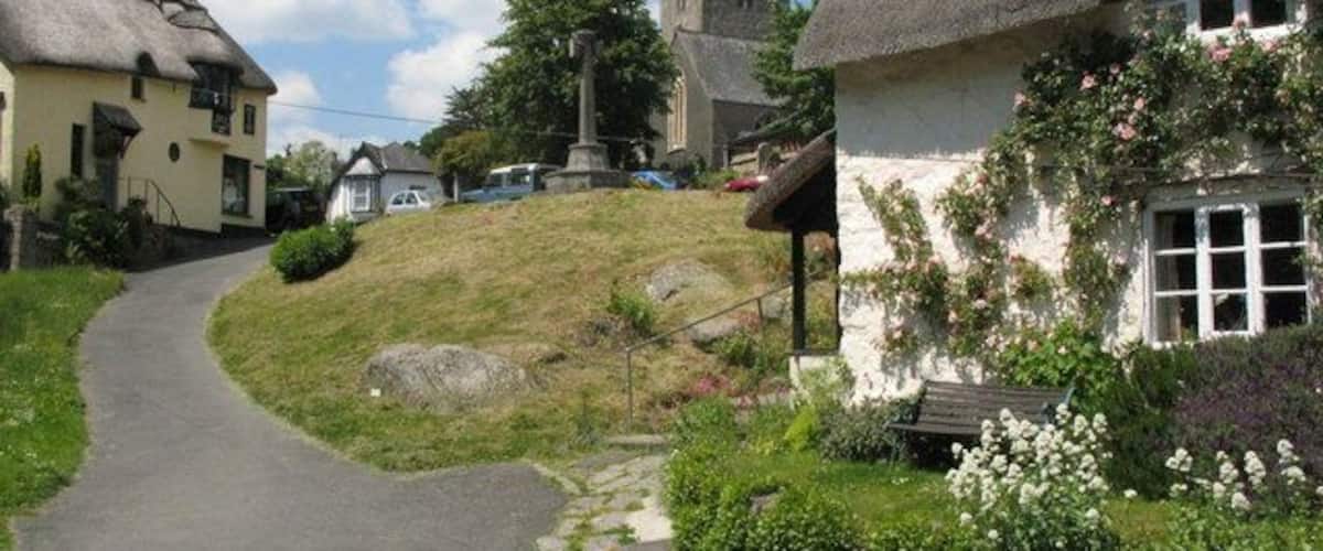 Lustleigh Village Green The green is quite small and contains the war memorial. The church is in the distance. The lane leads down (behind the photographer) to a small stream which runs under the disused rail bridge and on by the cricket field to Wreyland. The Primrose Cafe is on the left of the photograph.