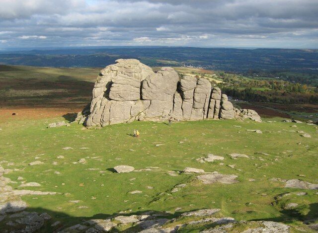 A large rock formation with a grassy foreground and a distant landscape.