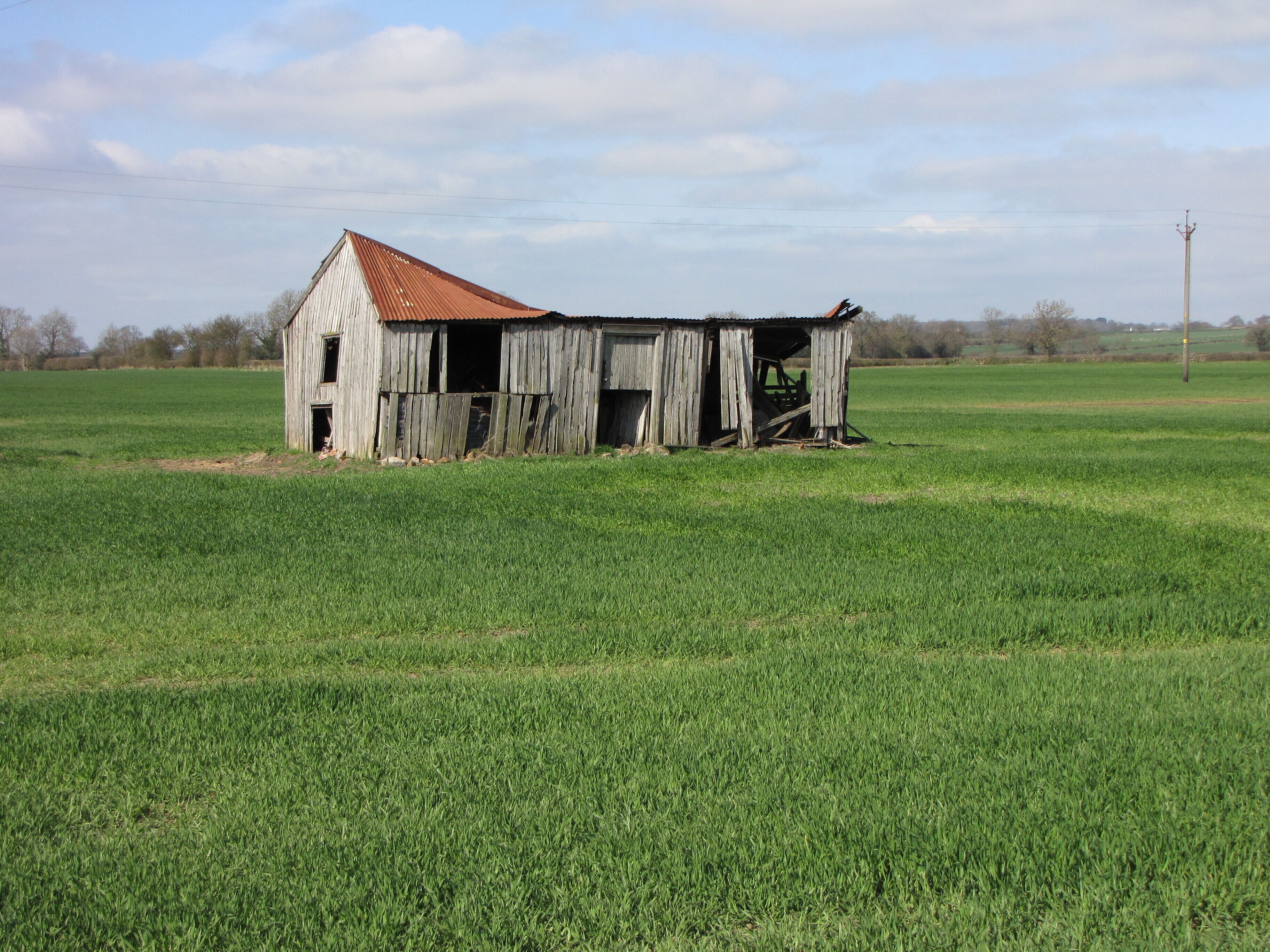 A dilapidated barn in a grassy field.