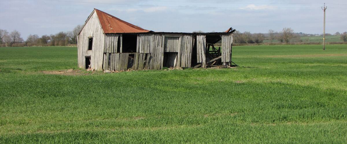 A dilapidated barn in a grassy field.