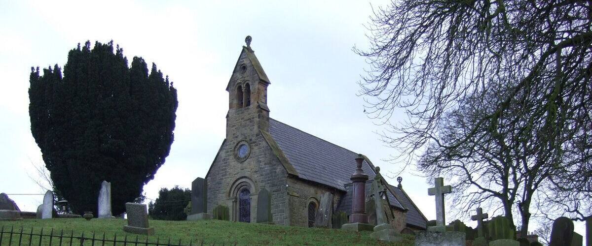 A church with a tall steeple and a stone wall in the foreground.