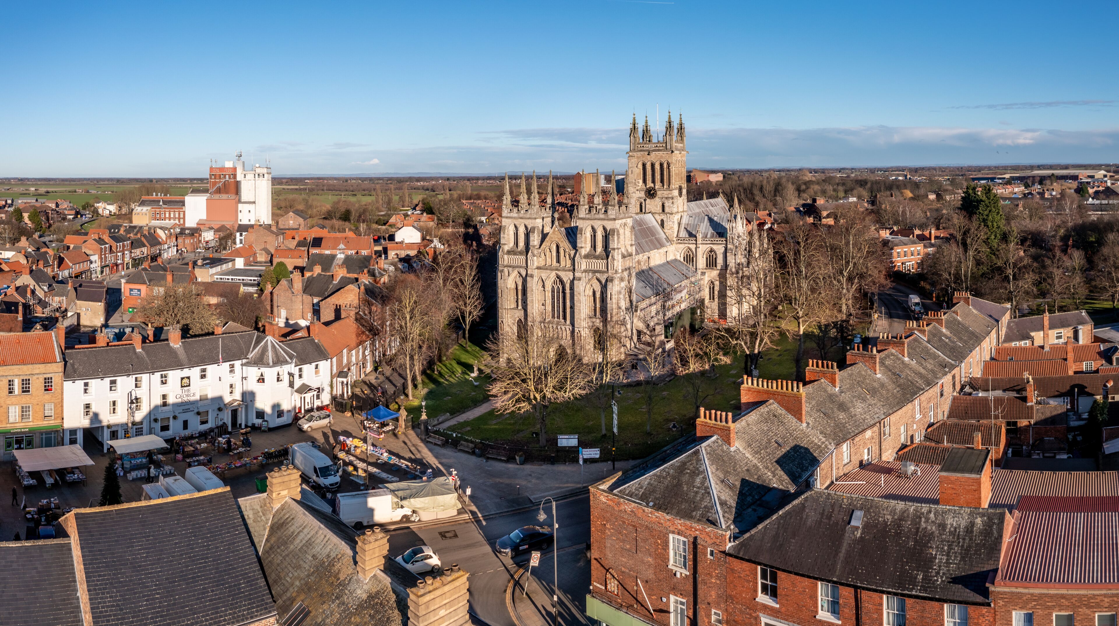 A historic cathedral with a clock tower, surrounded by a town with traditional architecture and a clear sky.