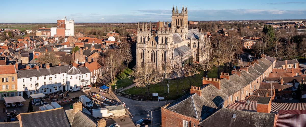 A historic cathedral with a clock tower, surrounded by a town with traditional architecture and a clear sky.