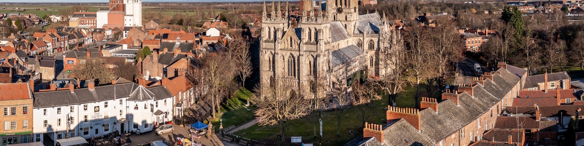 A historic cathedral with a clock tower, surrounded by a town with traditional architecture and a clear sky.