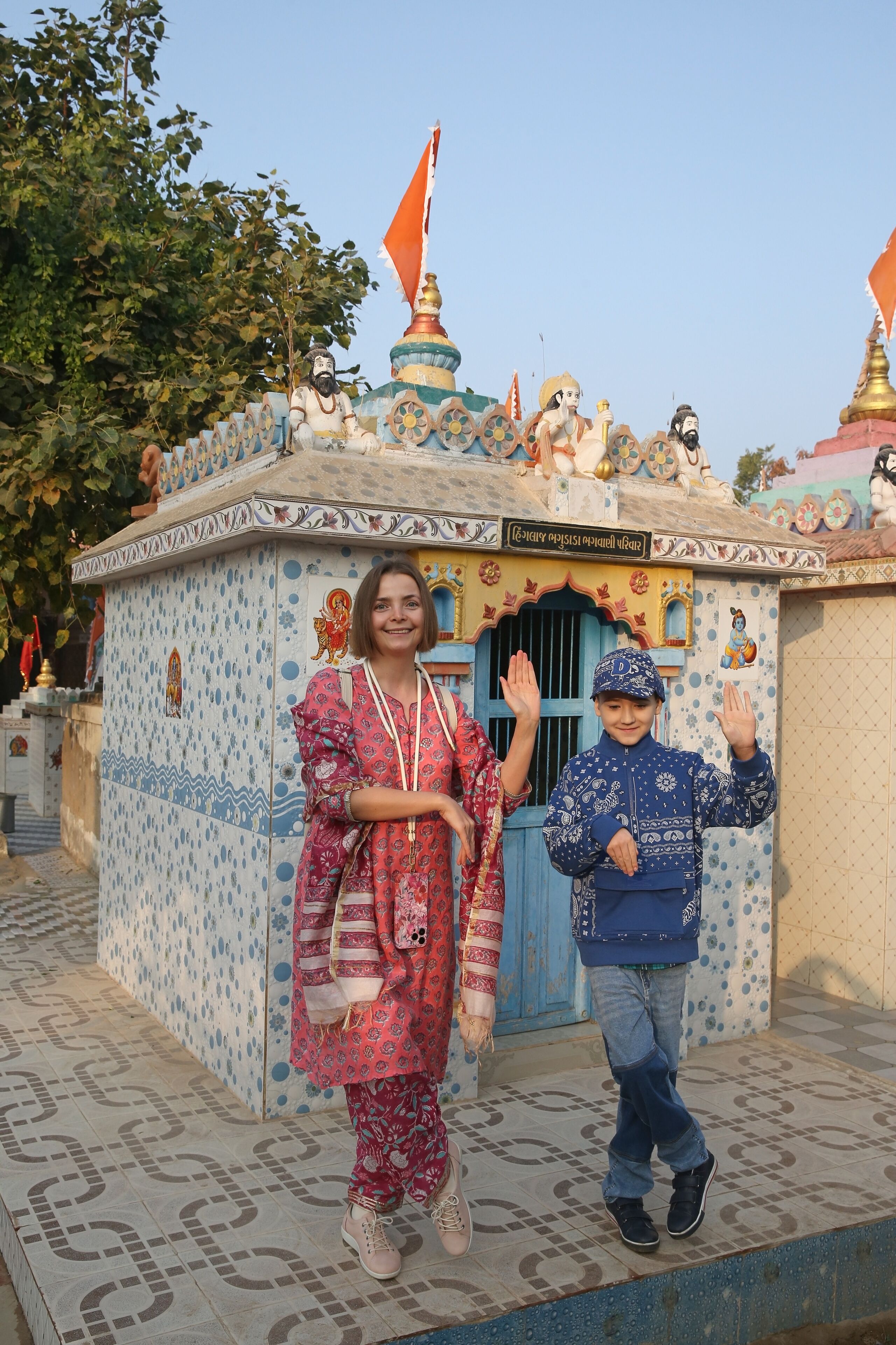 A temple with colorful patterns and flags, a child waving, and a woman in traditional attire.