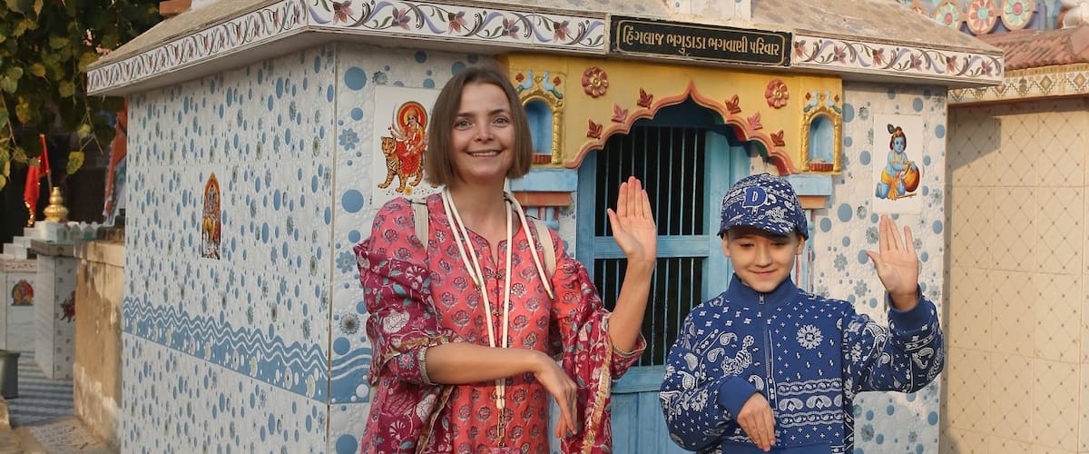 A temple with colorful patterns and flags, a child waving, and a woman in traditional attire.