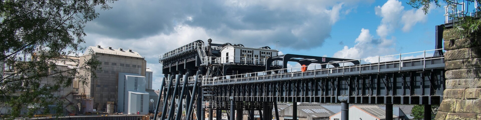 A historic industrial site with a large building, a pedestrian bridge, and a river.