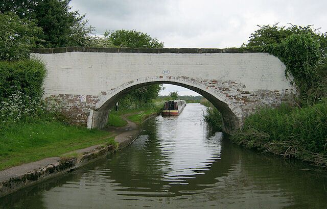 A narrow canal with a white brick bridge and a boat passing under it.