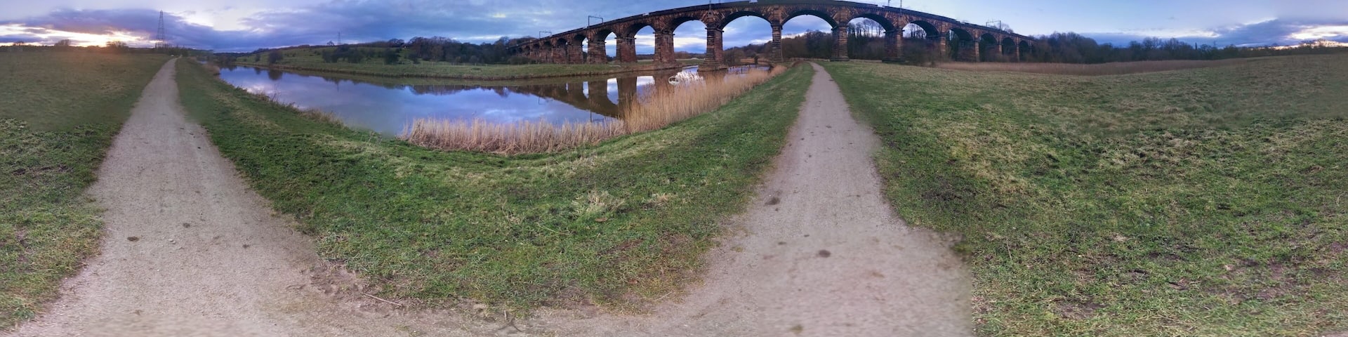 A viaduct over a river with a grassy path leading to it.