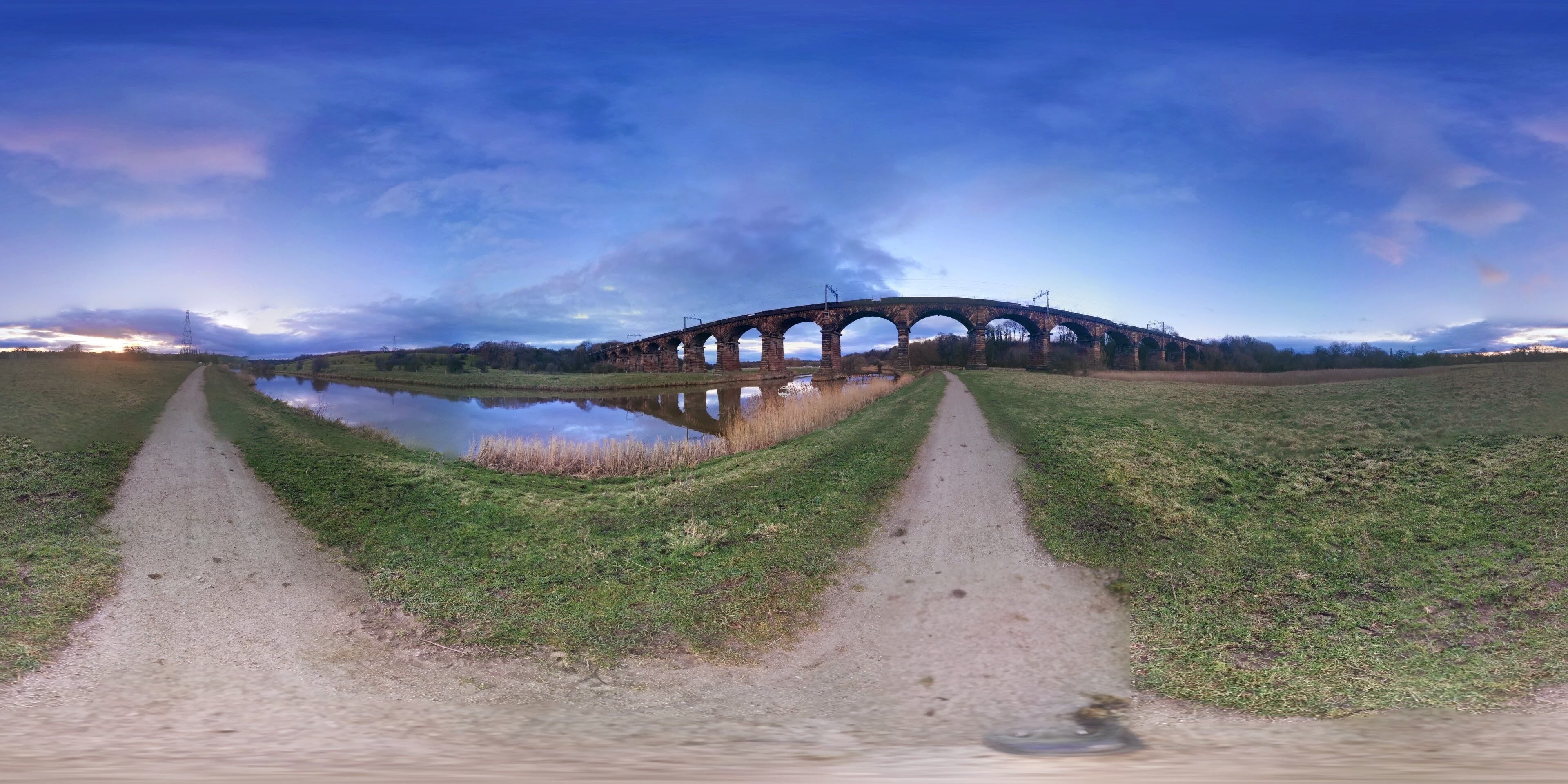A viaduct over a river with a grassy path leading to it.