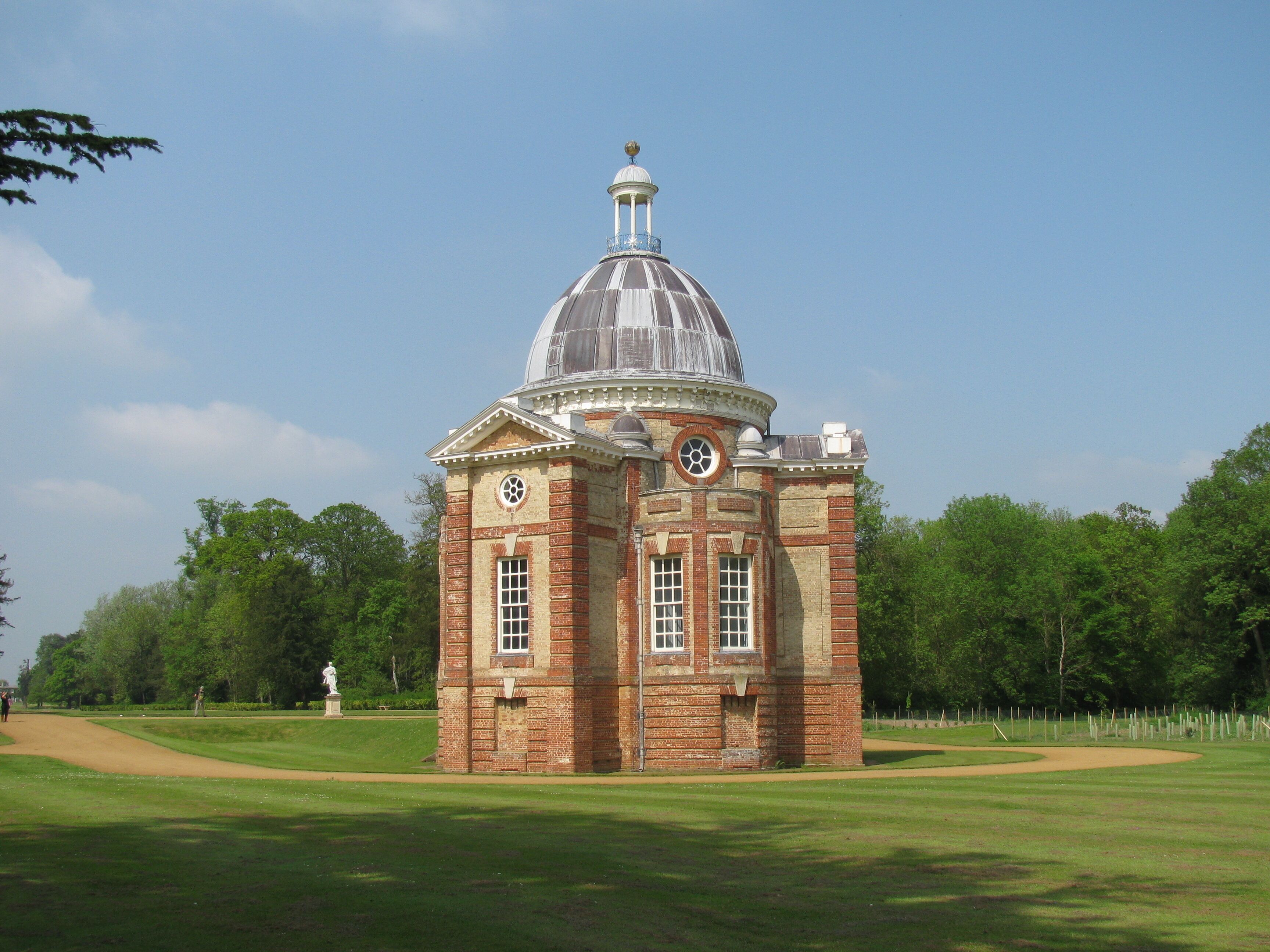 A historic brick building with a dome and clock tower, surrounded by a well-maintained lawn and trees.