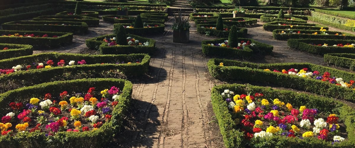 A formal garden with geometrically shaped flower beds and a central statue.