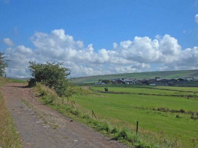 Moss Gate Road. Looking northeast towards Whitfield dairy farm from a point where Moss Gate Road ceases to border the Rushcroft area of Shaw. Crompton Moor can be seen on the skyline.