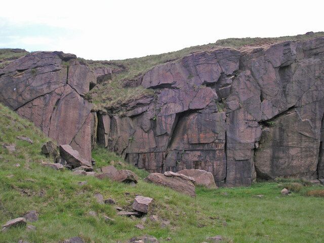 A large rock formation with a steep cliff face and scattered boulders.