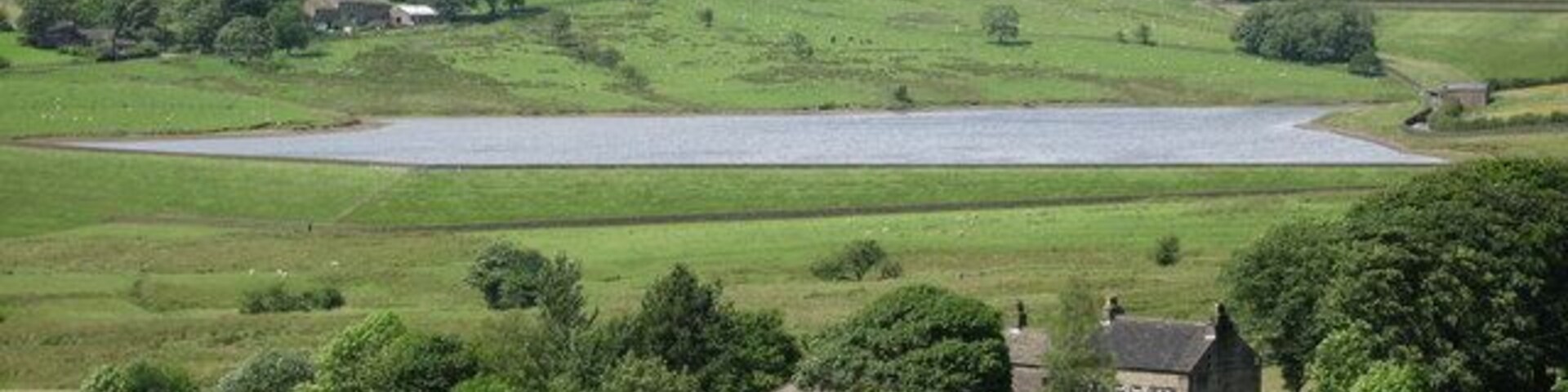 Un paisaje rural con colinas onduladas, un lago y casas dispersas.