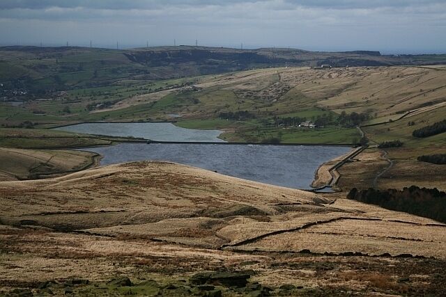 A lake surrounded by rolling hills and a distant view of wind turbines.