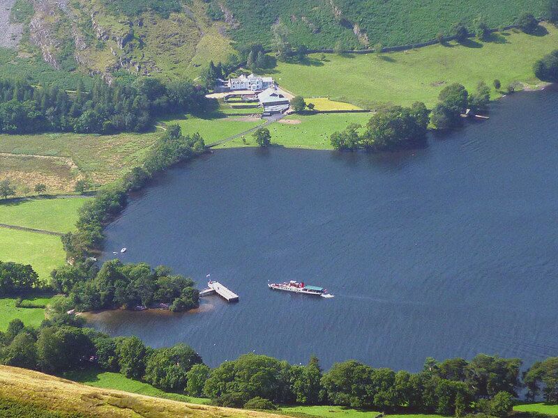 Un lago rodeado de colinas verdes, un muelle y una casa.