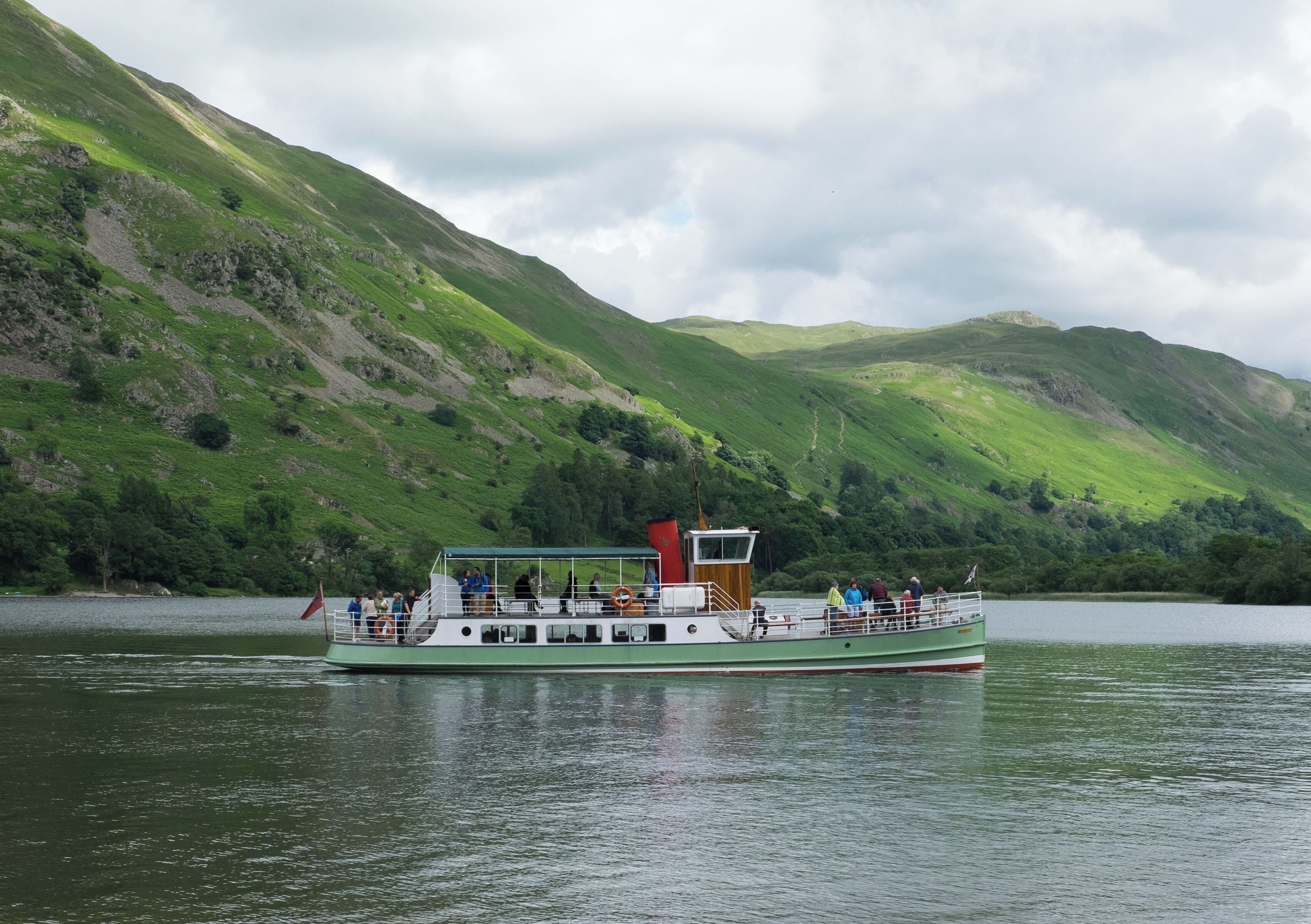 A green boat with passengers on a lake surrounded by green hills.