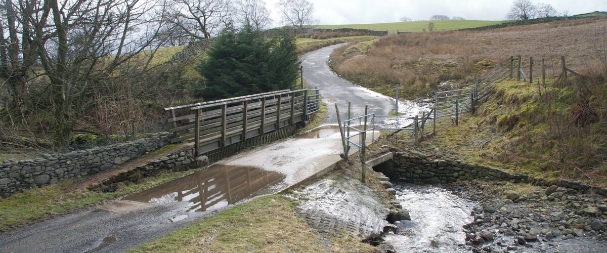 A rural road crossing a small stream with a wooden bridge.