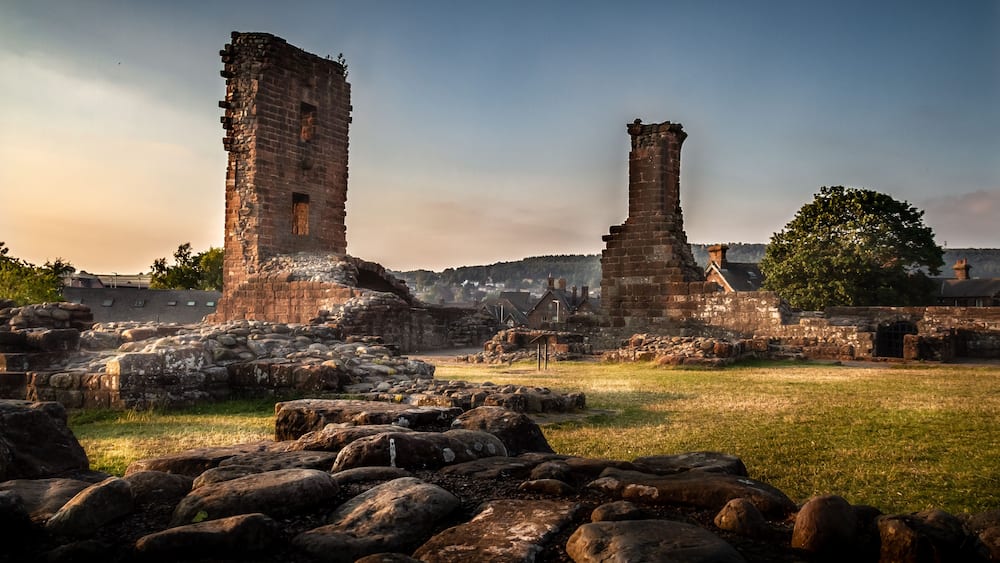 Des ruines anciennes en pierre, avec deux tours imposantes, entourées de rochers épars et d’un champ herbeux.