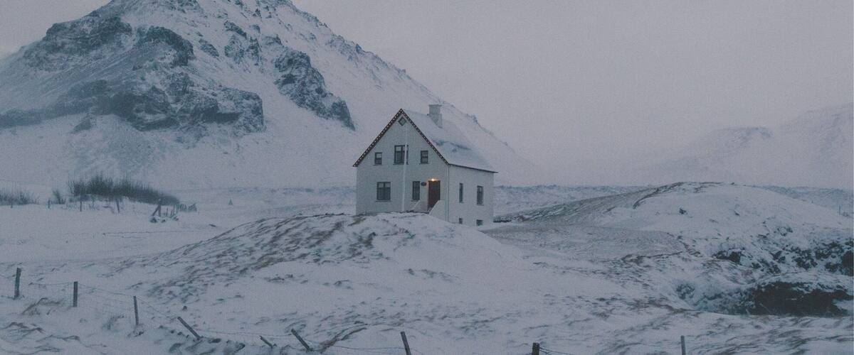 A snow-covered landscape with a white house and a mountain in the background.
