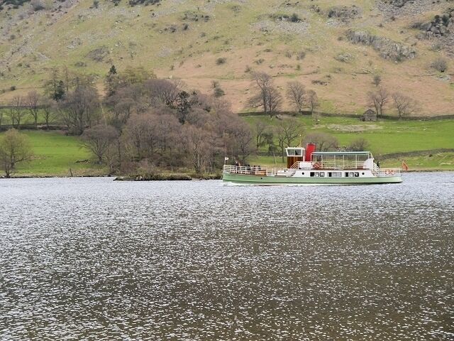 A riverboat on a calm river with a hilly landscape in the background.