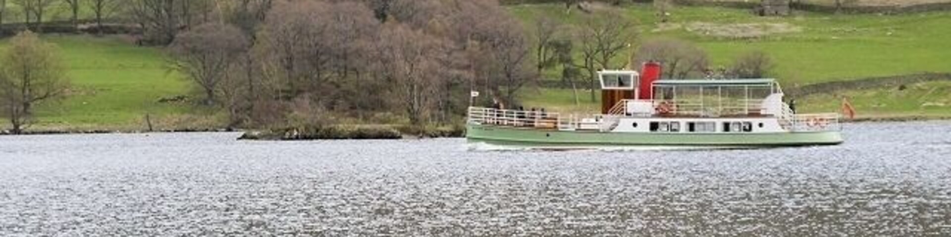 Um barco de passeio flutuando em um rio calmo, com uma paisagem montanhosa ao fundo.