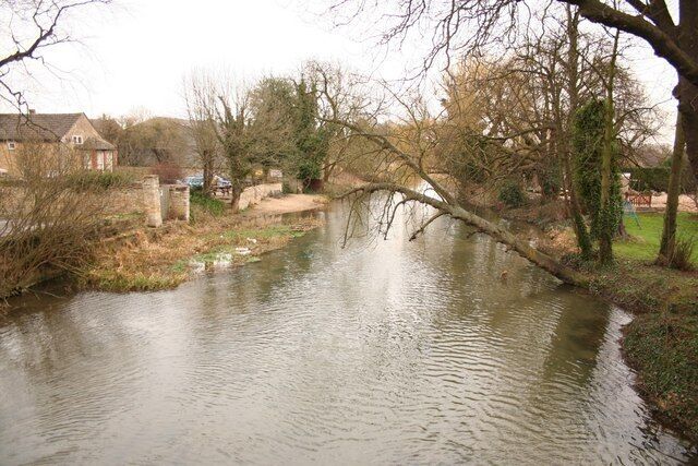 A calm river with a fallen tree, houses, and leafless trees in a rural setting.