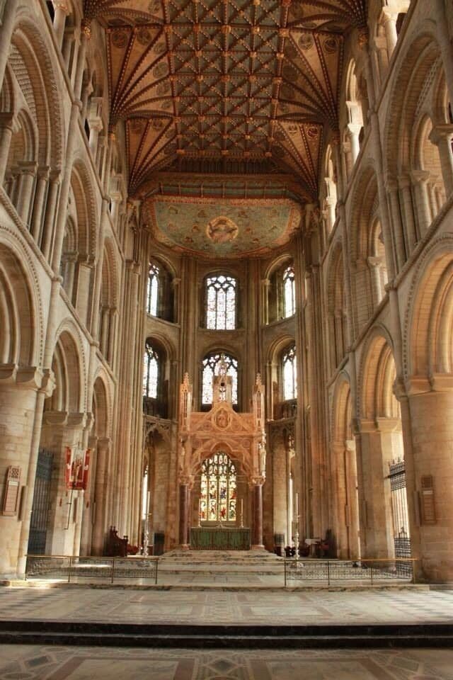 A cathedral interior with a high vaulted ceiling, large stained glass windows, and a central altar.