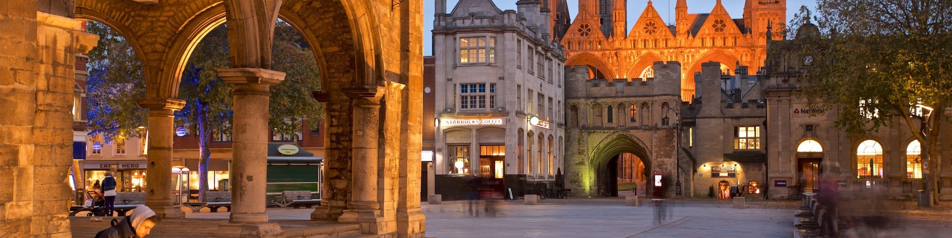A historic square with medieval architecture, including a prominent church with spires and a Starbucks.
