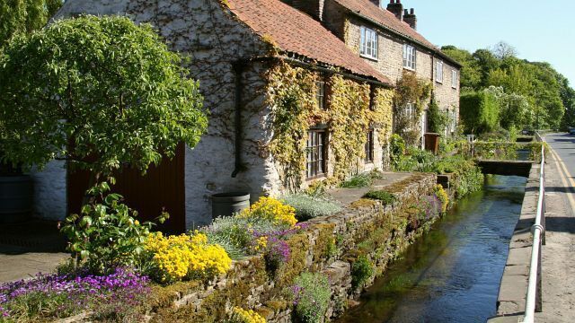Malton Gate. The stream, in this southerly facing photograph, is one of the water courses of Thornton Beck and is flowing in the direction of shot. The viewpoint of this photograph is opposite (on the other side of the road) an alley called Archway Lane, which joins Malton Gate at this point. The private dwellings in the photograph are Sunholme and Bishops Garth (farthest). On the same side of the road, and some 60metres south (ahead, on the cusp of the curve) is the entrance to 443025. For a more southerly (ahead) photograph of Malton Gate, click here 443027. For a more northerly (behind the viewpoint) photograph of Malton Gate, click here 442976.