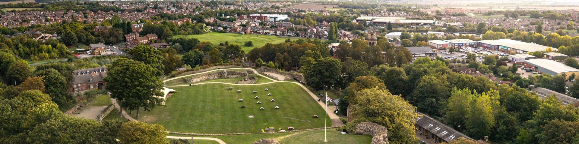 An aerial view of a historic castle surrounded by a park, with a residential area and industrial buildings in the background.