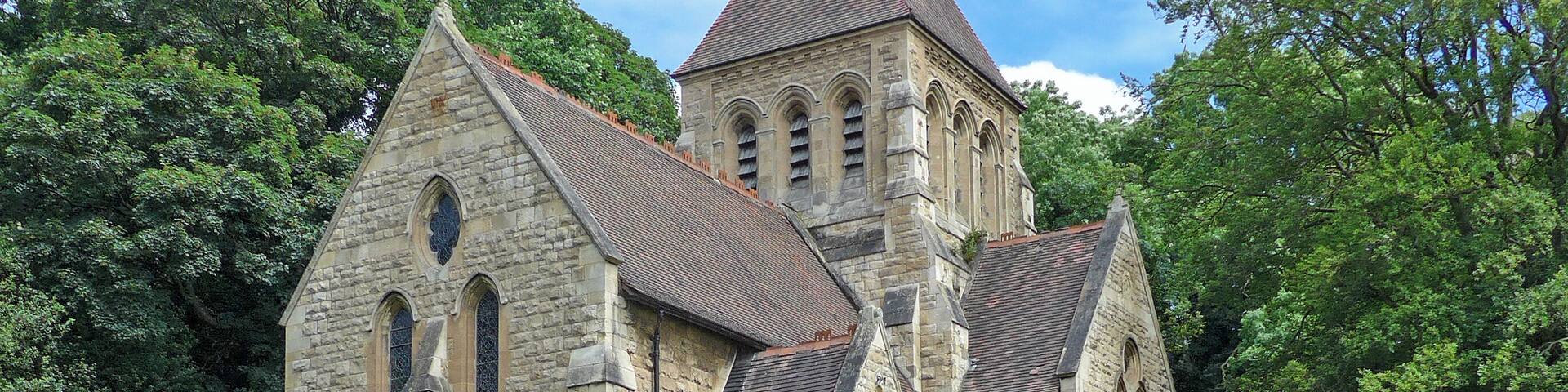A stone church with a pointed roof and arched windows, surrounded by a grassy field and a stone wall.