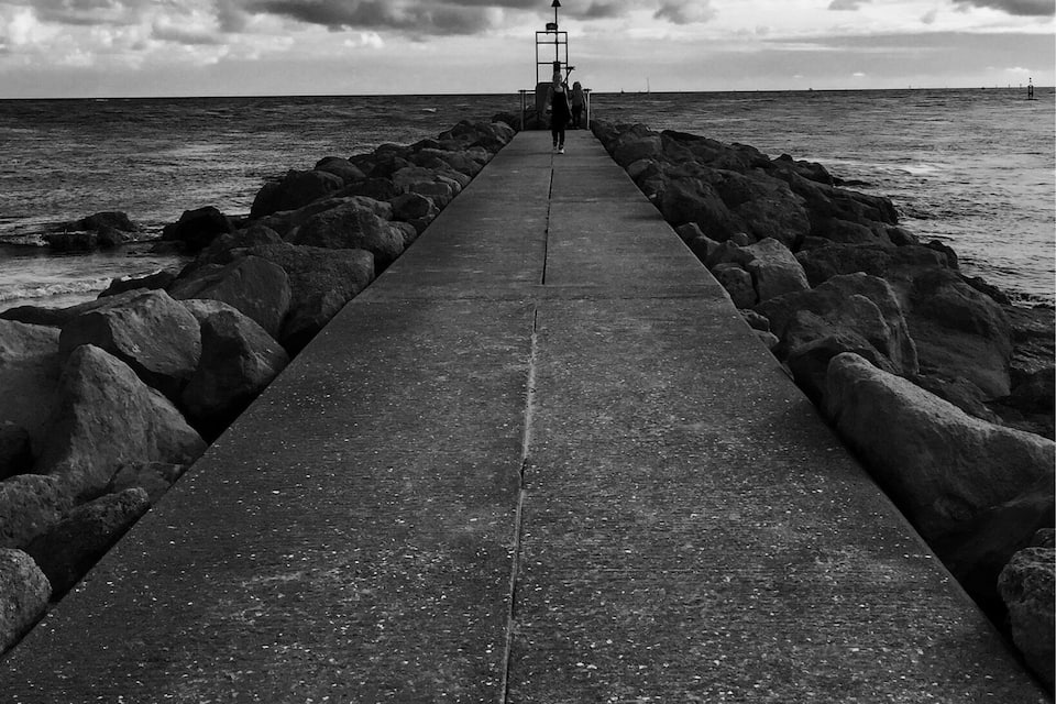 Un pilier de béton s’étendant dans la mer, avec de gros rochers de chaque côté, sous un ciel nuageux.