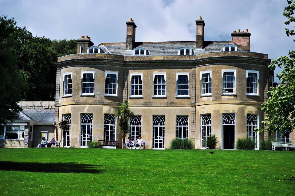 A historic building with a curved facade, large arched windows, and a well-maintained lawn in front.