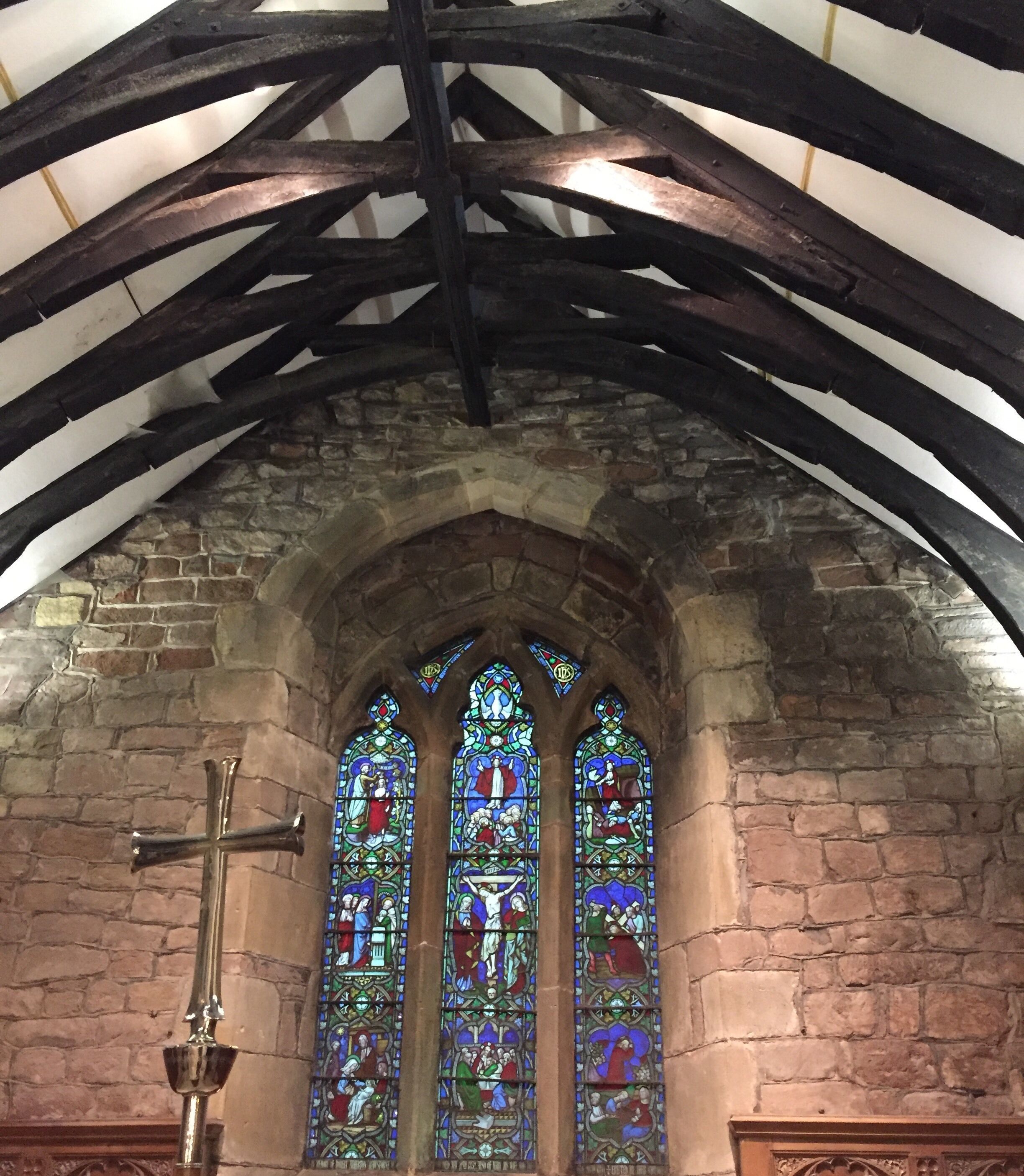 A church interior with a stone archway, stained glass windows, and a cross.