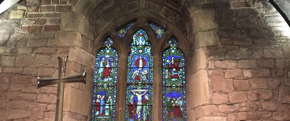 A church interior with a stone archway, stained glass windows, and a cross.