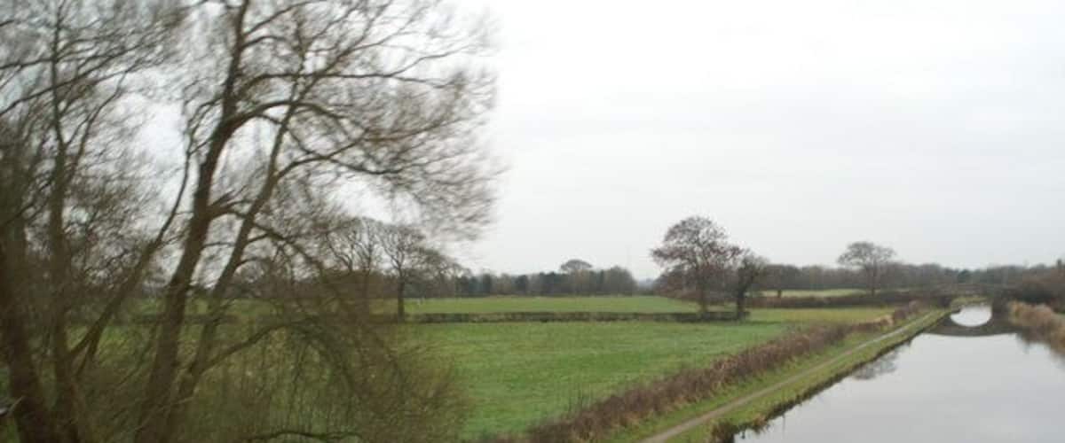 A narrow waterway flanked by grassy fields and leafless trees.