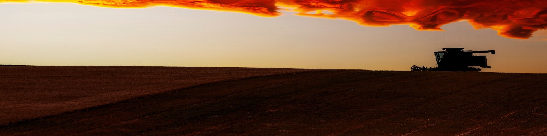 Dramatic colorful sky with combine in the field at harvest; East of Airdrie, Alberta, Canada