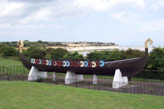 A Viking ship sculpture with colorful shields, set against a coastal backdrop.