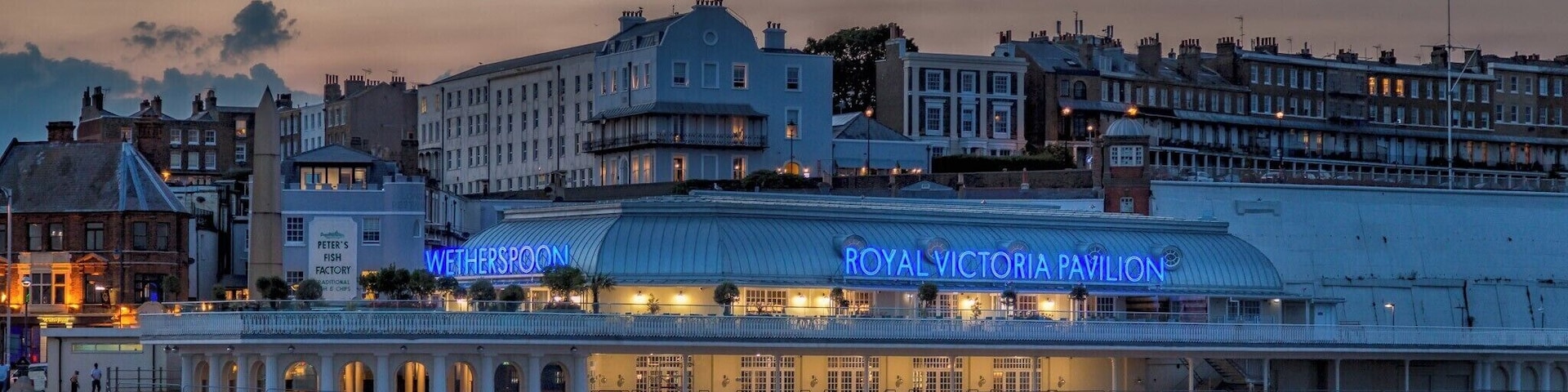 Le Royal Victoria Pavilion, reconnaissable à son enseigne néon bleue, la poissonnerie de Peter et les bâtiments historiques environnants.